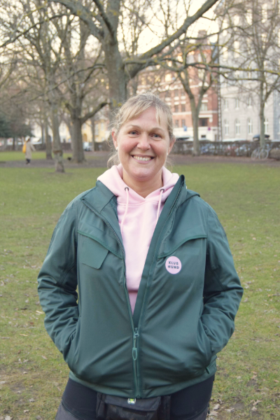 Billede af Ulla Elk, hundetræner hos klub hund, som står og smiler på træningspladsen på nørrebro